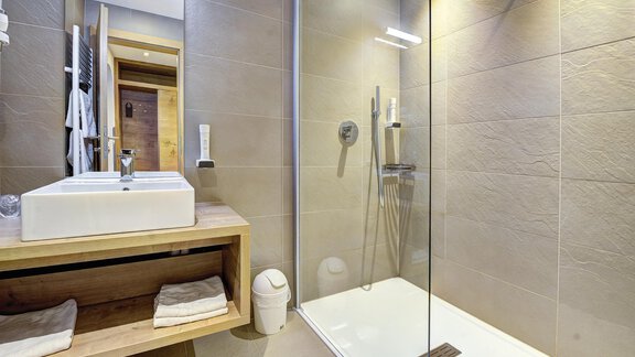 Ein modernes Badezimmer mit einer Dusche und einer stilvollen Waschbecken-Einheit aus Holz. Die Wände sind in neutralen Farben gehalten und schaffen eine elegante Atmosphäre. - Hotel Neue Post - Zwieselstein