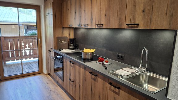 Eine moderne Küche mit Holzschränken und einem großen Fenster. - Landhaus Alpenjäger - Zwieselstein