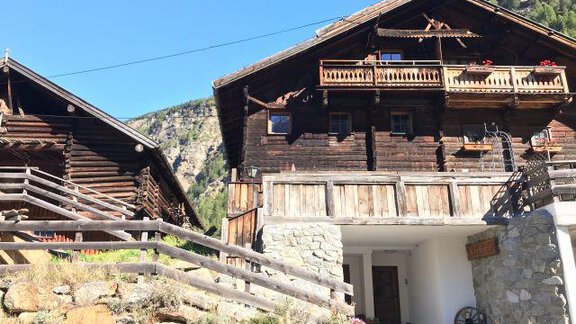 Ein traditionelles alpines Holzhaus mit einem Balkon und bunten Blumen. Im Hintergrund sind grüne Berge und ein blauer Himmel zu sehen. - The Private Chalet s’Tyrolia - Zwieselstein