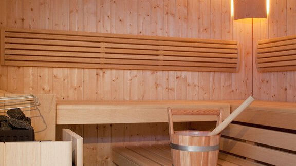 Eine gemütliche Sauna aus hellem Holz mit Bänken und einem Eimer für Wasser. Sanftes Licht sorgt für eine entspannende Atmosphäre. - Appartement Alpin - Sölden