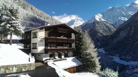 A cozy house in a snowy mountain landscape.  
Tall mountains and clear blue skies surround the scene. - Appartementhaus Fenderhof - Sölden