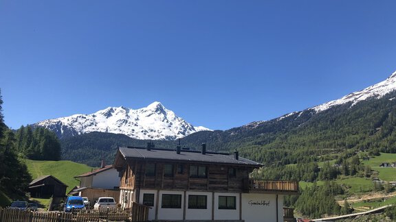 Eine malerische Berglandschaft mit schneebedeckten Gipfeln und grünen Wiesen. Im Vordergrund steht ein gemütliches Haus mit Balkonen. - Granbichlhof - Sölden