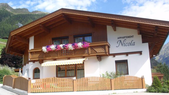 A cozy chalet with wooden cladding and colorful flowers at the windows. The apartment "Nicola" is located in a picturesque setting with mountains in the background. - Haus Nicola - Sölden