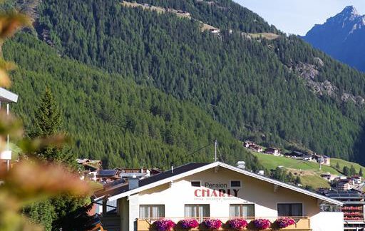 Ein idyllisches Bergdorf mit einem charmanten Hotel und blühenden Balkonblumen. Im Hintergrund erheben sich majestätische Berge unter einem klaren blauen Himmel. - Pension Charly - Sölden