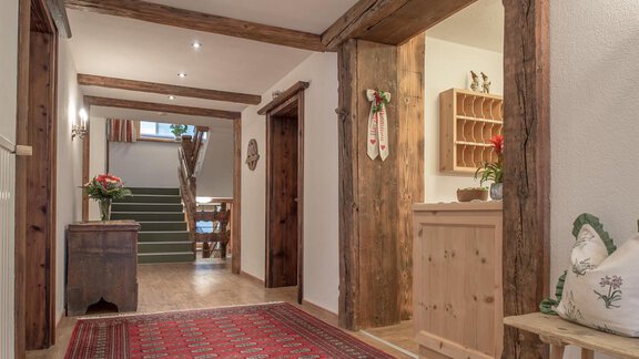 Ein einladender Flur mit Holzbalken und einem Orientteppich. Auf der linken Seite befindet sich eine Empfangstheke und eine Treppe, die nach oben führt. - Pension Michael - Obergurgl 