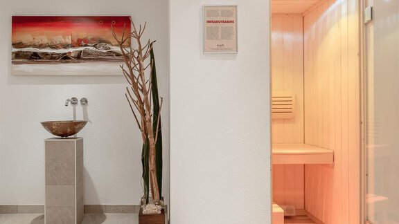 Ein moderner Wellnessbereich mit einer eleganten Waschschüssel und einem Zugang zur Sauna. An der Wand hängt ein dekoratives Bild, das die entspannende Atmosphäre ergänzt. - Pension Michael - Obergurgl 