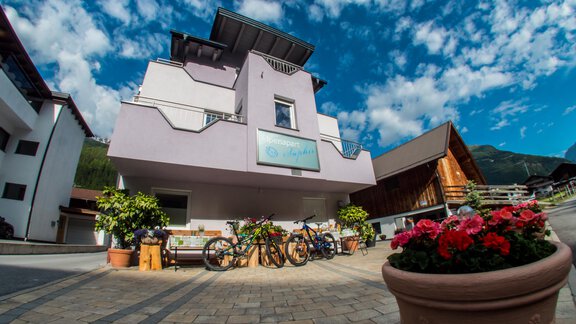 A modern building with a clear sky in the background. Bicycles and flowers adorn the entrance. - Alpenapart Saphir - Sölden