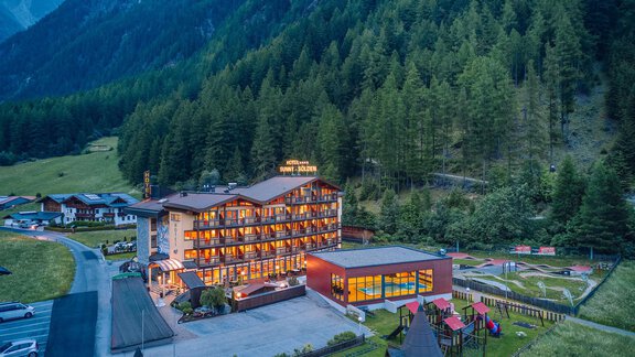 A cozy hotel nestled in a green mountainous landscape. The facade of the building radiates warm light and invites relaxation. - Hotel Sunny Sölden - Sölden