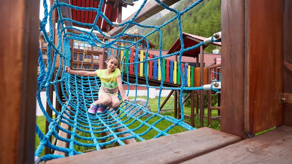 A child is playing on a climbing frame with a net. The surroundings are green and friendly, ideal for outdoor activities. - Hotel Sunny Sölden - Sölden