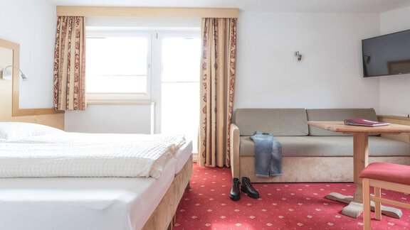 Ein helles Zimmer mit einem Doppelbett und einem Balkon. Es gibt ein Schlafsofa, einen Tisch und einen Fernseher an der Wand. - Landhaus Fiegl - Sölden