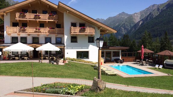 Ein schönes Hotel mit Balkon und Sonnenschirmen im Freien. Im Vordergrund befindet sich ein Pool, umgeben von einer malerischen Berglandschaft. - Pension Waldesruh - Sölden
