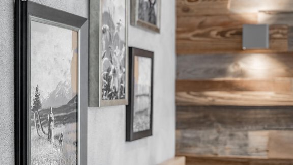 Ein moderner Innenraum mit schwarz-weißen Bildern in Rahmen an einer grauen Wand. Im Hintergrund sind Holzelemente sichtbar, die dem Raum Gemütlichkeit verleihen. - Residenz Allegra - Sölden