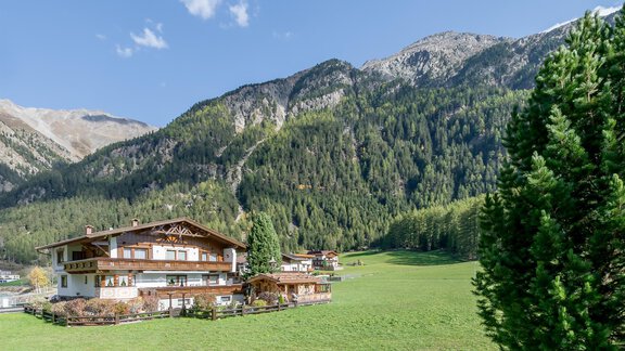 Ein malerisches Alpenhaus umgeben von grünen Wiesen und hohen Bergen. Der Himmel ist klar und sonnig, was eine ruhige Atmosphäre schafft. - Apart Wiesengrund - Sölden