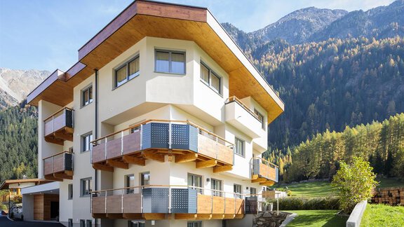 A modern residential building with wooden balustrades and large windows. In the background, majestic mountains and green forests can be seen. - Haus Madeleine - Sölden