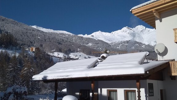 A snowy landscape with a house and snow-covered mountains in the background. The sky is clear and blue. - Michls Hoamat Appartement - Sölden