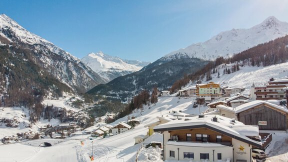 A picturesque winter landscape with snow-covered mountains and charming houses. The clear blue sky perfectly complements the alpine village. - Apart Sonnhof - Sölden