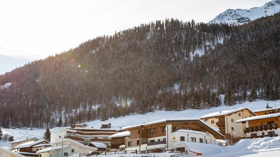 A picturesque winter landscape with snow-covered hills and a charming village. The sun shines over the mountains and illuminates the houses. - Apart Sonnhof - Sölden