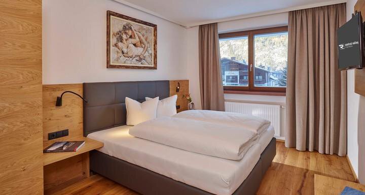 Ein modernes Schlafzimmer mit einem Doppelbett und Holzmöbeln. Große Fenster lassen viel Licht herein und bieten einen Blick auf die Umgebung. - Alpenappartement Central Valley Penthouse - Längenfeld