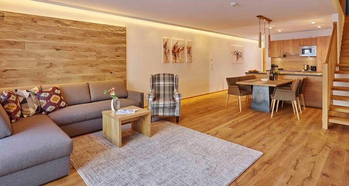 Ein modernes Wohnzimmer mit einem gemütlichen Sofa und einem Holzregal. Der angrenzende Essbereich ist hell und einladend gestaltet. - Alpenappartement Central Valley Penthouse - Längenfeld