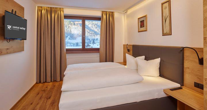 Ein modernes Zimmer mit zwei Betten und einem großen Fenster. Die Einrichtung ist in warmen Holz- und Farbnuancen gehalten. - Alpenappartement Central Valley Penthouse - Längenfeld