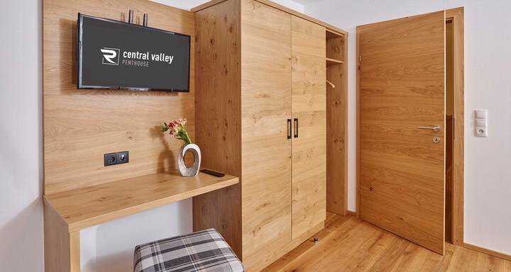 Ein modernes Zimmer mit Holz-Möbeln und einem Fernseher an der Wand. Die Einrichtung umfasst einen Schreibtisch und einen Kleiderschrank. - Alpenappartement Central Valley Penthouse - Längenfeld
