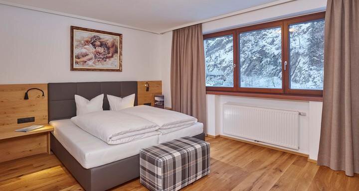Ein modernes Schlafzimmer mit einem Doppelbett und Holzmöbeln. Das Zimmer hat große Fenster mit Blick auf die schneebedeckte Landschaft draußen. - Alpenappartement Central Valley Penthouse - Längenfeld