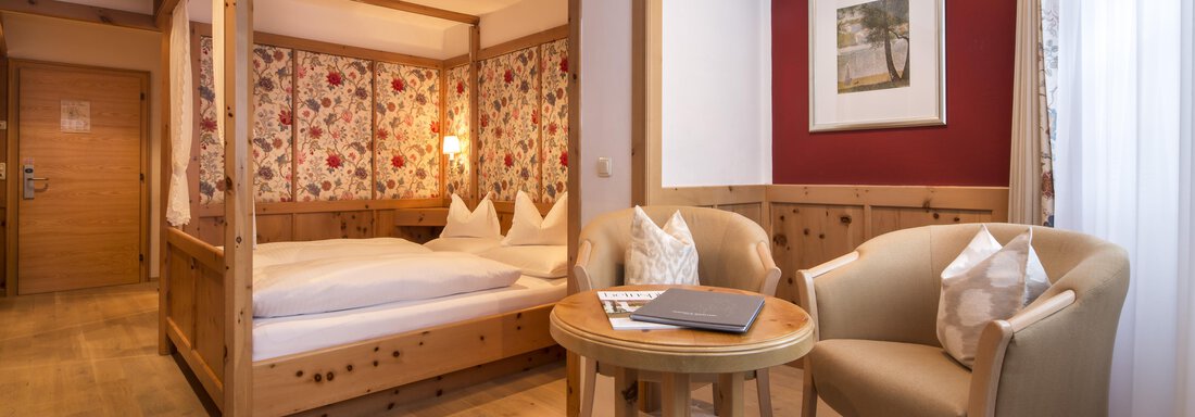 Hotel-Bergwelt-Obergurgl-Doppelzimmer-A2 | © Art & Relax Hotel Bergwelt (CC BY) A cozy hotel room with a wooden bed and floral design. There is a small table and two chairs, as well as warm light. - Art & Relax Hotel Bergwelt - Obergurgl