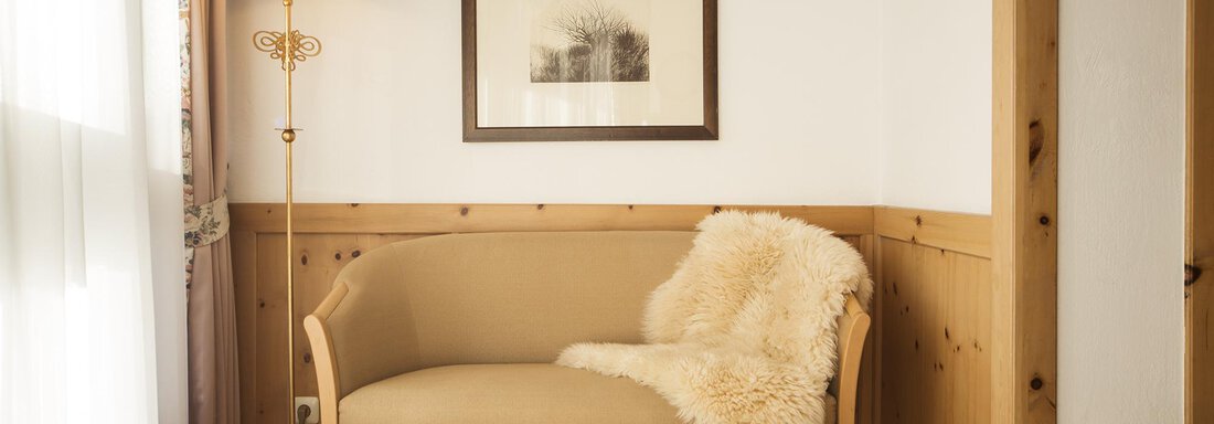 Juniorsuite A3/A4 | © Art & Rekax Hotel Bergwelt (CC C) A cozy seating area with a beige sofa and a snuggly blanket. Next to the sofa is a floor lamp, and a framed artwork hangs on the wall. - Art & Relax Hotel Bergwelt - Obergurgl