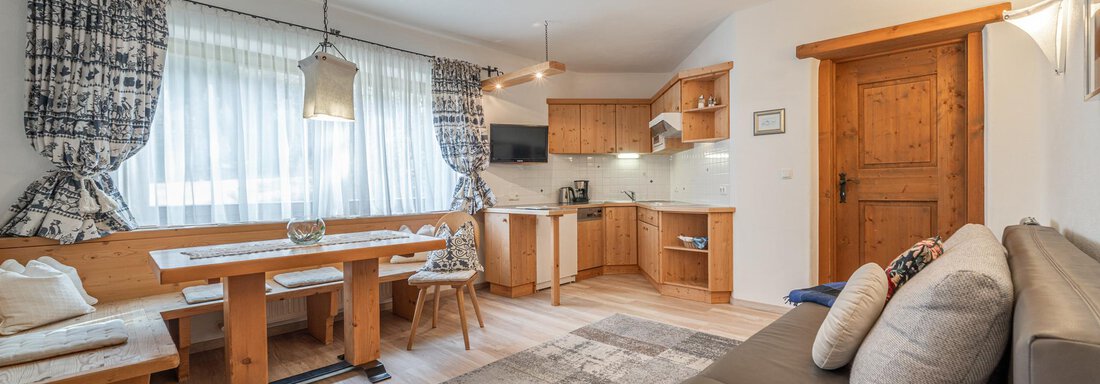 Ein gemütlicher Wohnraum mit einer modernen Küche und einem Esstisch aus Holz. Große Fenster sorgen für viel Licht und eine einladende Atmosphäre. - Ferienwohnung Alt Poschach - Obergurgl 
