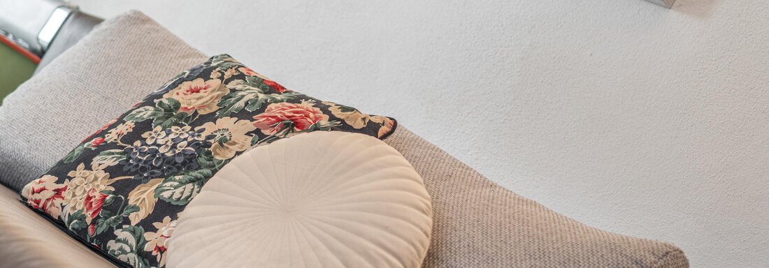 Ein gemütliches Sofa mit zwei Kissen, eines mit floralem Muster und das andere rund. An der Wand hängt ein Bild. - Ferienwohnung Alt Poschach - Obergurgl 