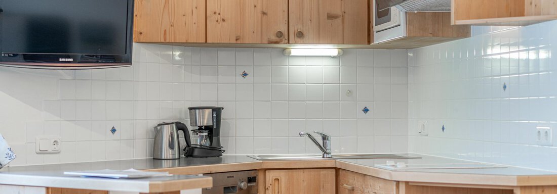 Eine moderne Küche mit Holzschränken und einem integrierten Fernseher. Die Ausstattung umfasst eine Kaffeemaschine und eine Spüle. - Ferienwohnung Alt Poschach - Obergurgl 