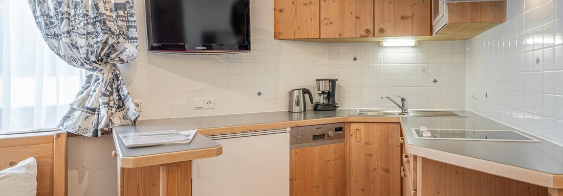Eine moderne Küche mit Holzmöbeln und einem großen Fenster. Es gibt einen Fernseher, eine Küchenzeile und verschiedene Geräte. - Ferienwohnung Alt Poschach - Obergurgl 