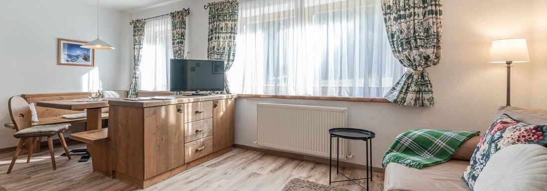 Ein gemütliches Wohnzimmer mit einem Sofa, einem Tisch und einem Fernseher. Helle Vorhänge und Holzdetails schaffen eine einladende Atmosphäre. - Ferienwohnung Alt Poschach - Obergurgl 