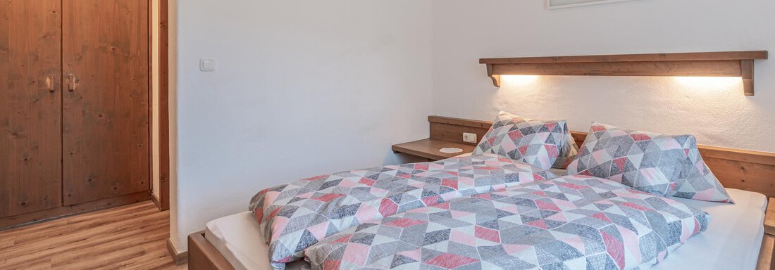 Ein gemütliches Schlafzimmer mit einem großen Bett und bunten Bettwäsche. Der Raum hat Holzverkleidungen und eine ruhige Atmosphäre. - Ferienwohnung Alt Poschach - Obergurgl 