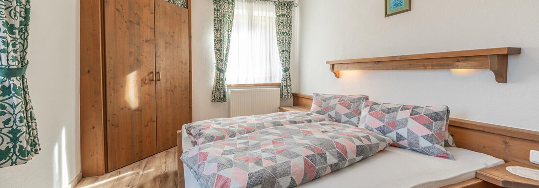 Ein gemütliches Schlafzimmer mit einem Doppelbett und bunten Decken. Der Raum hat helles Holz und grüne Vorhänge, die für eine einladende Atmosphäre sorgen. - Ferienwohnung Alt Poschach - Obergurgl 