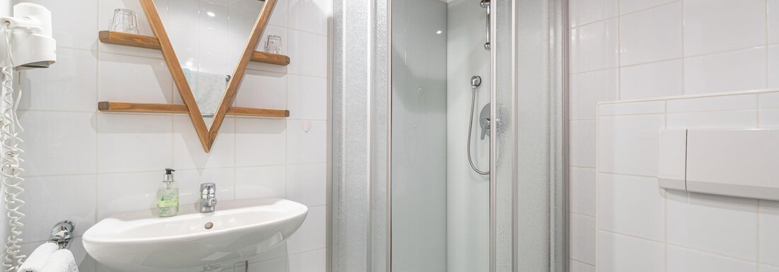 Ein modernes Badezimmer mit einer Dusche aus Glas und einem eleganten Spiegel. Die Wände sind weiß gefliest, und der Boden ist in einem dunklen Grün. - Ferienwohnung Alt Poschach - Obergurgl 