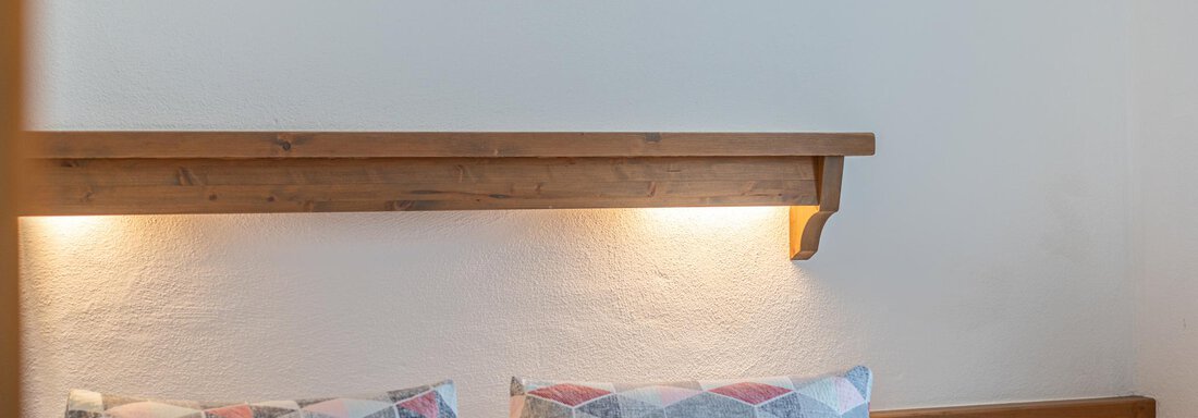 Ein gemütliches Schlafzimmer mit einem Doppelbett und bunten Kissen. An der Wand hängt ein klar strukturiertes Kunstwerk. - Ferienwohnung Alt Poschach - Obergurgl 