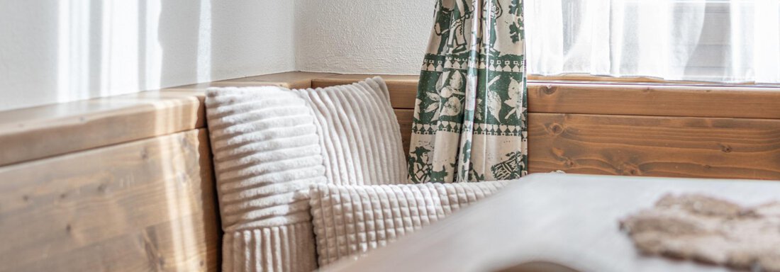Ein gemütlicher Essbereich mit Holzmöbeln und bequemen Kissen. Helle Vorhänge lassen viel Tageslicht hereinfallden. - Ferienwohnung Alt Poschach - Obergurgl 