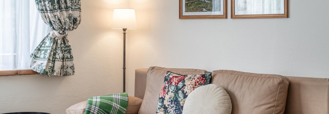 Ein gemütliches Wohnzimmer mit einem braunen Sofa und bunten Kissen. An der Wand hängen zwei Bilder, und ein Tischleuchte sorgt für angenehmes Licht. - Ferienwohnung Alt Poschach - Obergurgl 