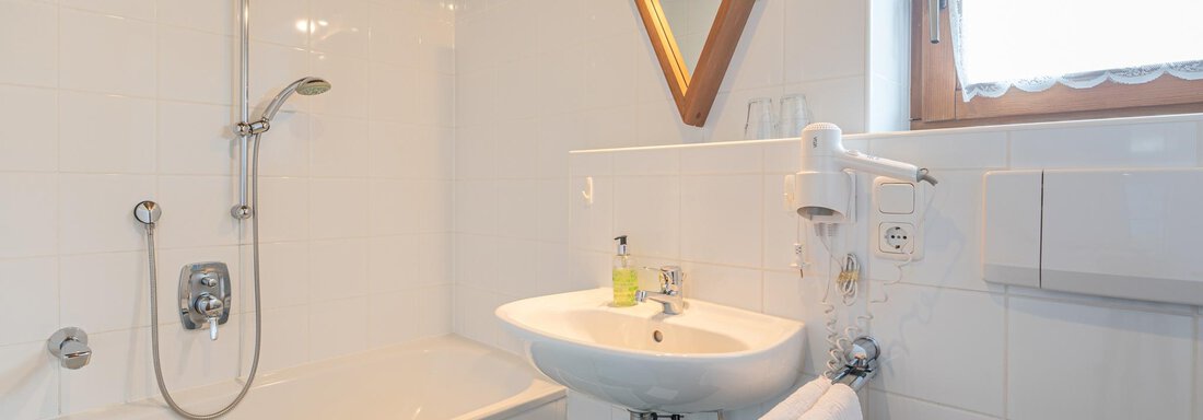 Ein helles Badezimmer mit einer Badewanne und einem Waschbecken. Die Wände sind weiß gefliest und ein großer Spiegel ist angebracht. - Ferienwohnung Alt Poschach - Obergurgl 