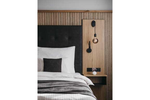 A modern bedroom with an elegant bed and a wooden wall. The bedside lamp radiates a warm atmosphere. - The Crystal VAYA Unique - Obergurgl 