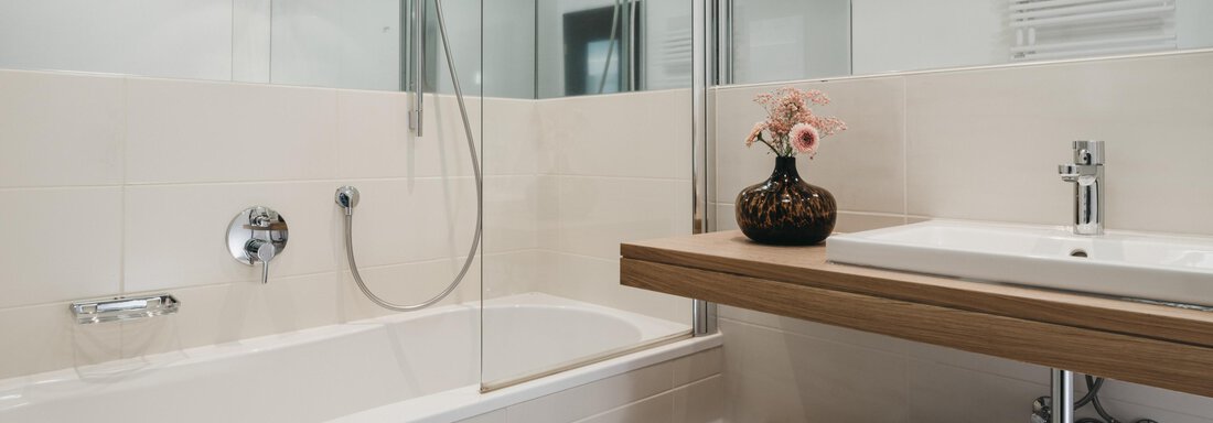 A modern bathroom with a bathtub and a shower. On the shelf are a sink and a flower in a vase. - The Crystal VAYA Unique - Obergurgl 