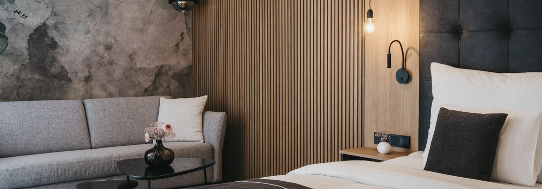 A modern bedroom with a large bed and a cozy sofa. The walls are stylishly decorated with wood paneling and concrete elements. - The Crystal VAYA Unique - Obergurgl 