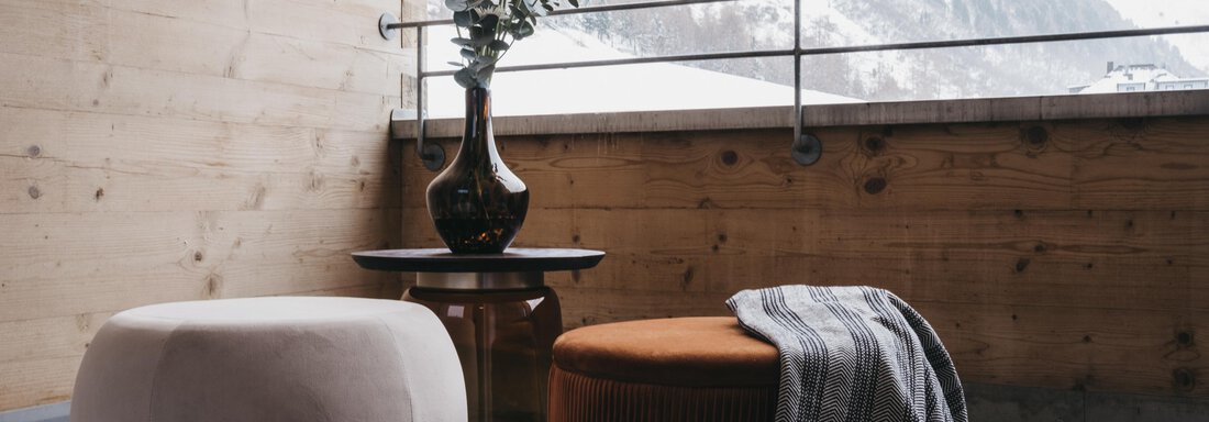 A cozy balcony with two stools and a small table. In the background, snow-covered mountains and a plant in a vase are visible. - The Crystal VAYA Unique - Obergurgl 