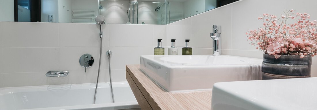 A modern bathroom with a large bathtub and two sinks. The room design is bright and minimalist with mirrors and plants. - The Crystal VAYA Unique - Obergurgl 