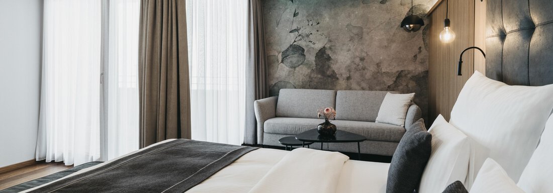 A modern hotel room with a large bed and a cozy seating area.  
Large windows provide plenty of daylight and a pleasant atmosphere. - The Crystal VAYA Unique - Obergurgl 