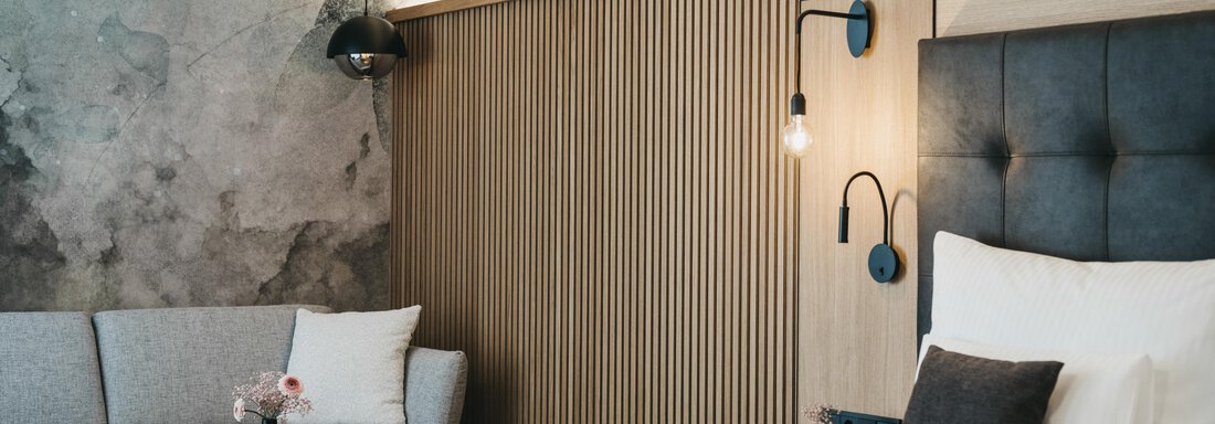 A modern bedroom with a large bed and an elegant sofa. The walls are designed with wood and gray concrete, creating a stylish atmosphere. - The Crystal VAYA Unique - Obergurgl 