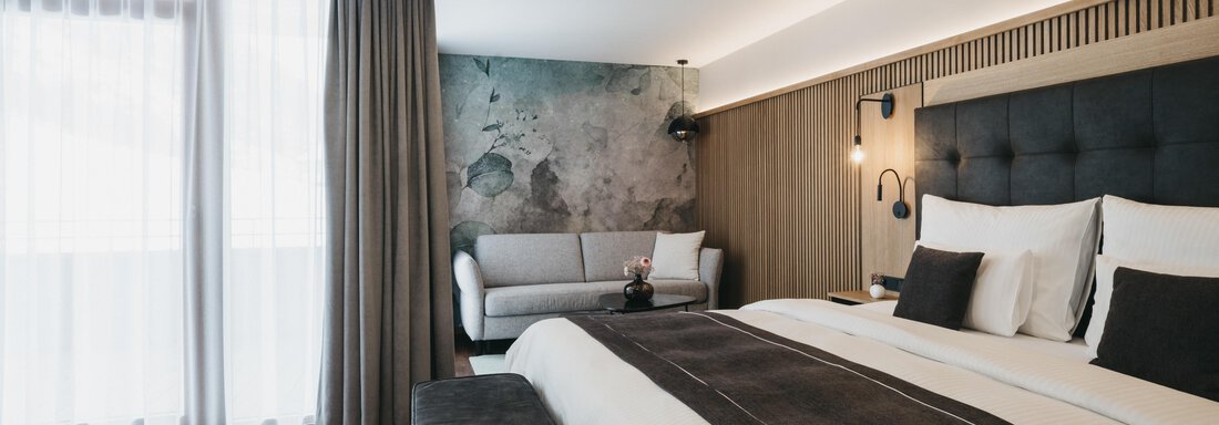 A modern hotel room with a large bed and a cozy sitting area. Bright curtains create a pleasant atmosphere. - The Crystal VAYA Unique - Obergurgl 