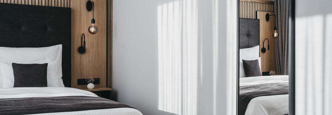 A modern bedroom with a comfortable bed and stylish wooden elements. A large mirror reflects natural light and creates a bright atmosphere. - The Crystal VAYA Unique - Obergurgl 