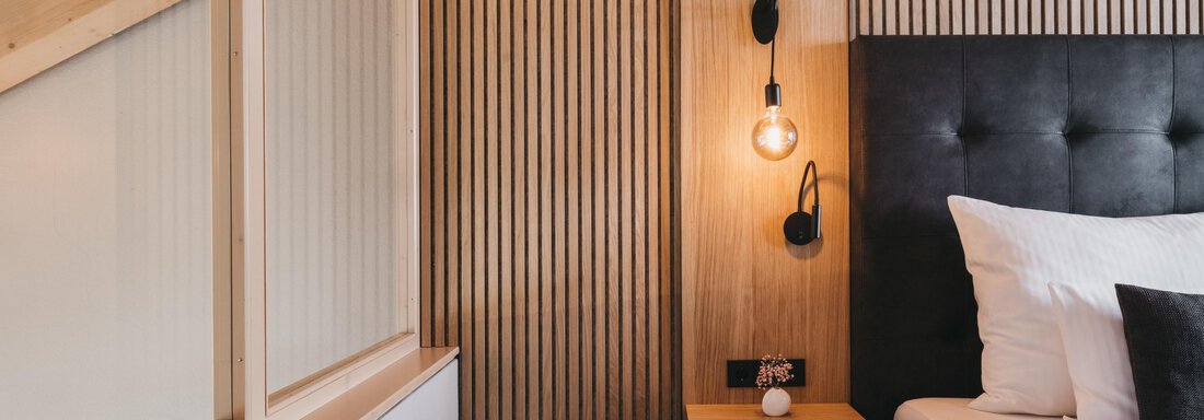 A modern bedroom with a comfortable bed and decorative wooden walls. Soft lighting creates an inviting atmosphere. - The Crystal VAYA Unique - Obergurgl 